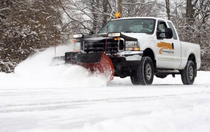 Crooked Tree Nursery snow plow truck clearing snow from a commercial parking lot during a Michigan winter storm.