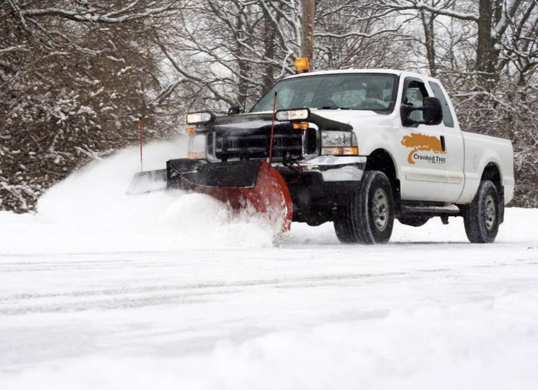 Crooked Tree Nursery snow plow truck clearing snow from a commercial parking lot during a Michigan winter storm.
