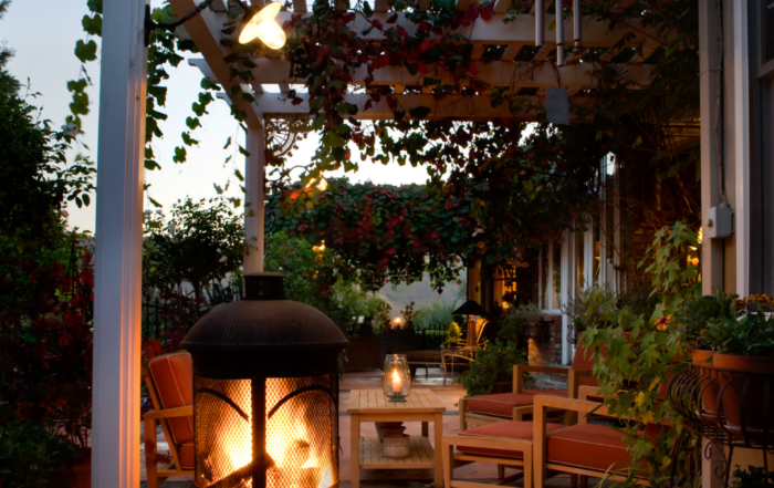 Covered patio with pergola, outdoor fire feature, seating area, and landscape lighting creating a cozy outdoor living space