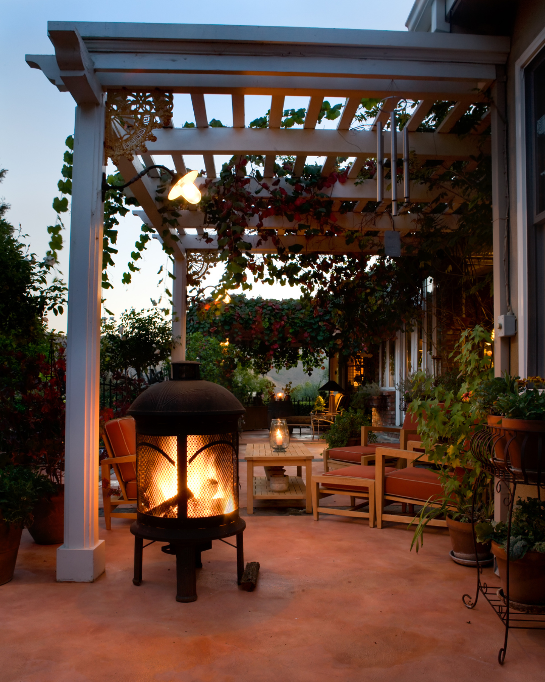 Covered patio with pergola, outdoor fire feature, seating area, and landscape lighting creating a cozy outdoor living space